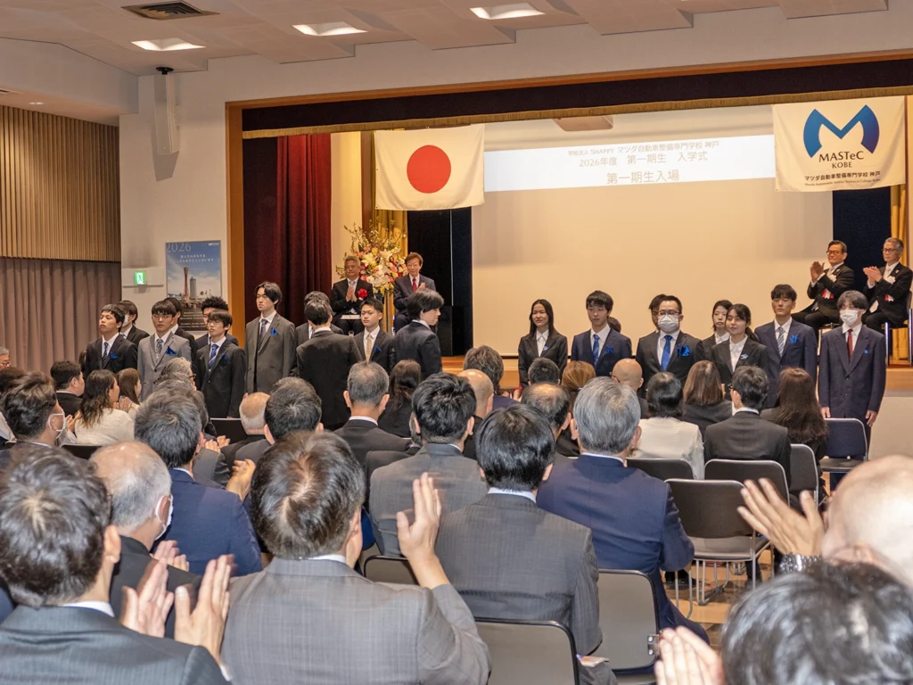マツダ自動車整備専門学校（神戸）の入学式。真新しいスーツ姿の第一期生（開拓者）たちを拍手で迎えている。